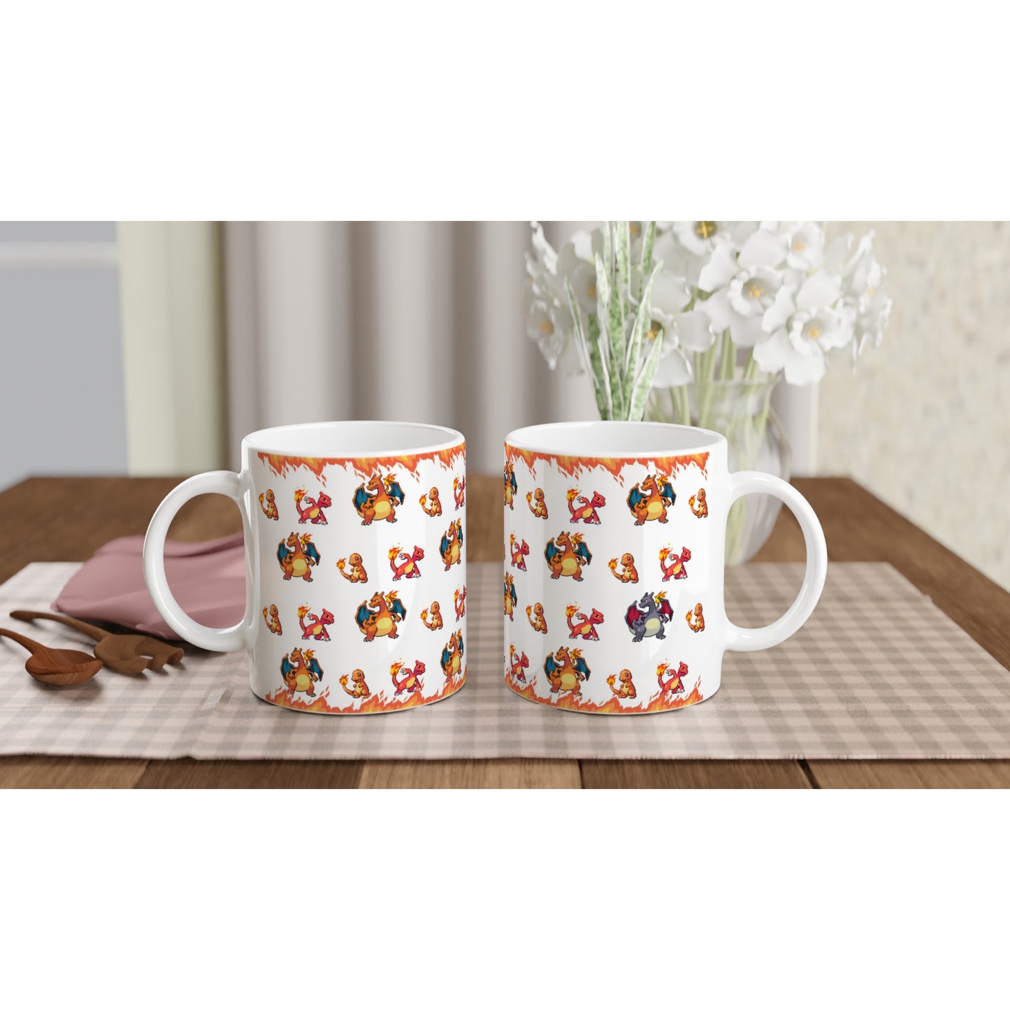 Two white mugs featuring a fire-themed pixel art design of Charmander, Charmeleon, Charizard, and shiny Charizard, placed on a checkered tablecloth with decorative white flowers in the background.