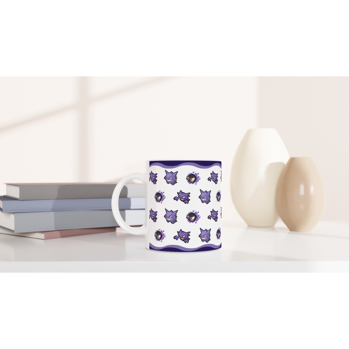 White Pokémon mug featuring Gengar, Haunter, and Gastly pixel art design, placed on a modern desk with books and vases for home decor.