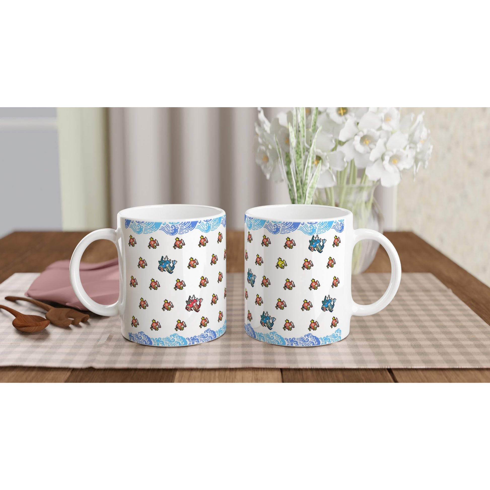 Set of two Pokémon mugs with pixel art of Magikarp and Gyarados, displayed on a cozy table setting with flowers, showcasing a blue wave border design.