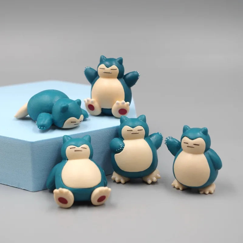 Set of adorable Snorlax figurines in various poses, including sitting, waving, and sleeping, displayed on a light blue block with a neutral gray background.